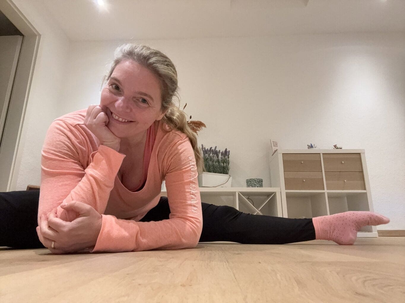 Pilates Mit Anna Pilates Anna sitzt im Grätschsitz mit aufgestützen Ellbogen und lächelt