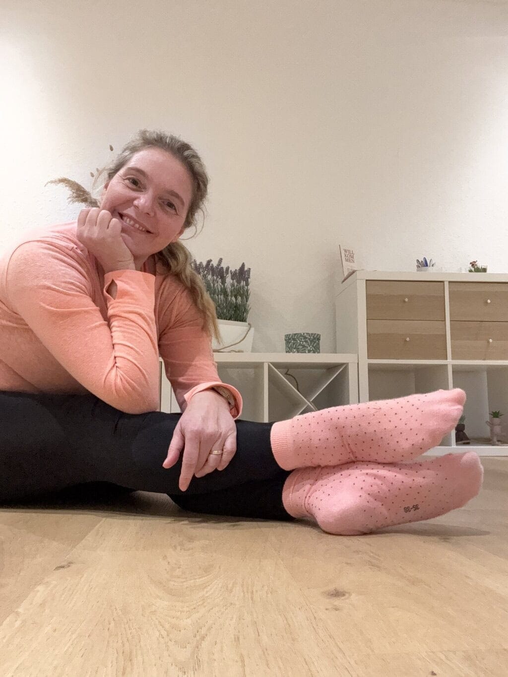 die Pilates Anna Pilatesanna mit ausgestreckten übereinander geschlagenen Beinen auf dem Boden und lächelt